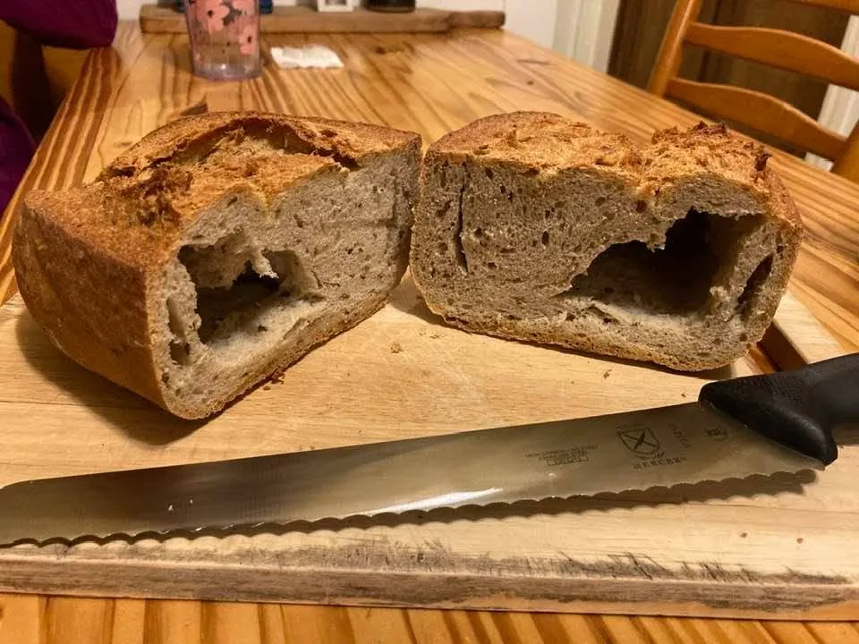 Two halves of a badly tunneled loaf of bread on a cutting board, next to a serrated bread knife